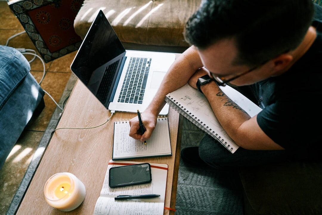 Person taking notes next to an open laptop